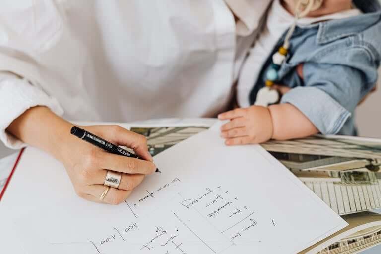 A mother working on notes while holding her baby close, illustrating multitasking.